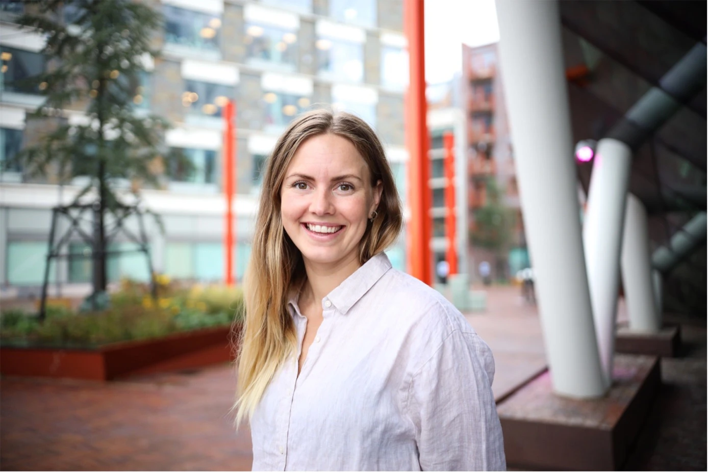 Elin Lundblad står utanför entrén till Center för innovation i Oceanhamnen, med träd, vita pelare och glasfasader i bakgrunden