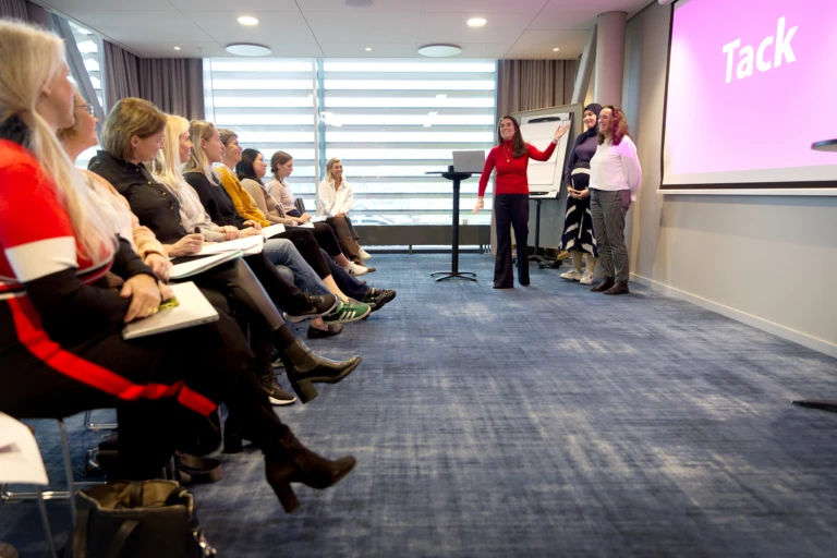 Tre kvinnor presenterar framför ett 20-tal personer i en publik i ett konferensrum