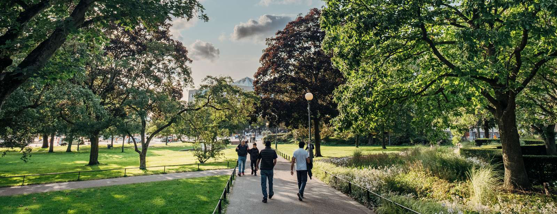Människor promenerar i den gröna och soliga stadsparken i Helsingborg.
