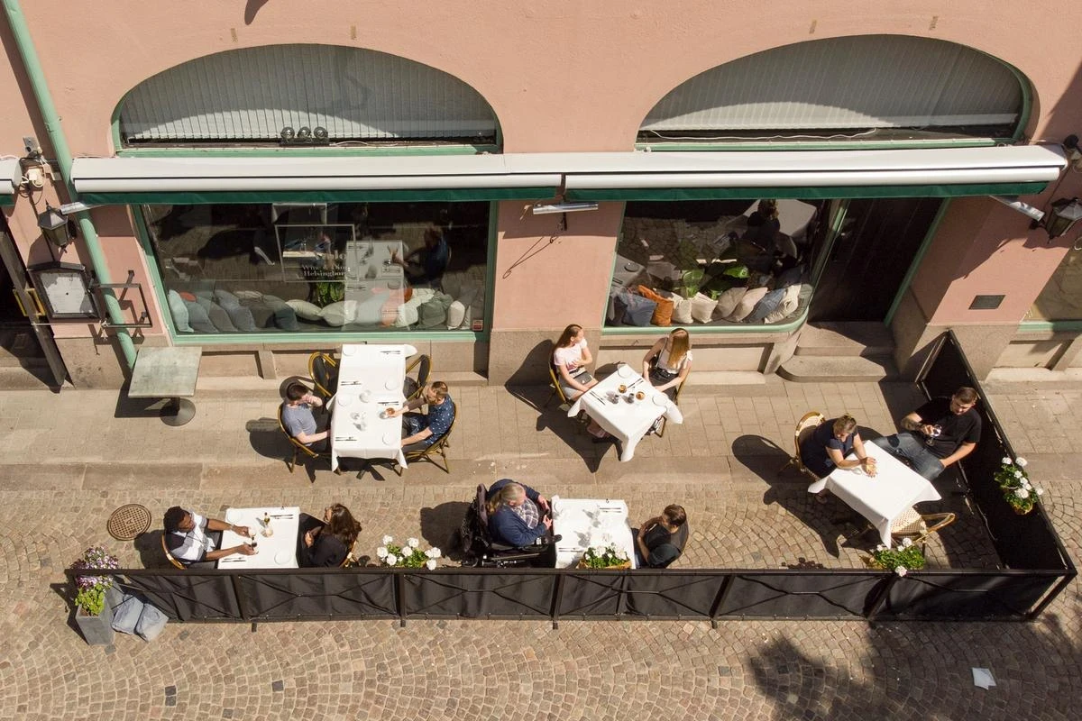 Personer sitter på en uteservering på Bruksgatan. Uteserverigen, med bord och stolar, har fotograferats uppifrån.