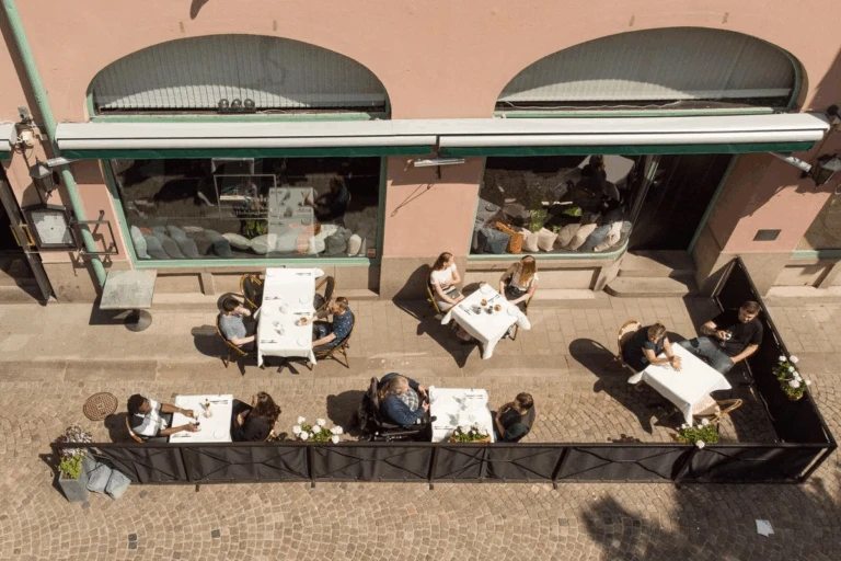 Personer sitter på en uteservering på Bruksgatan. Uteserverigen, med bord och stolar, har fotograferats uppifrån.