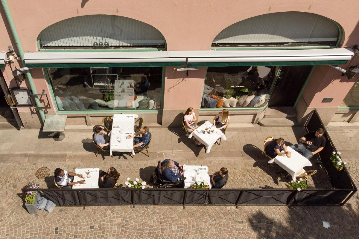Personer sitter på en uteservering på Bruksgatan. Uteserverigen, med bord och stolar, har fotograferats uppifrån.