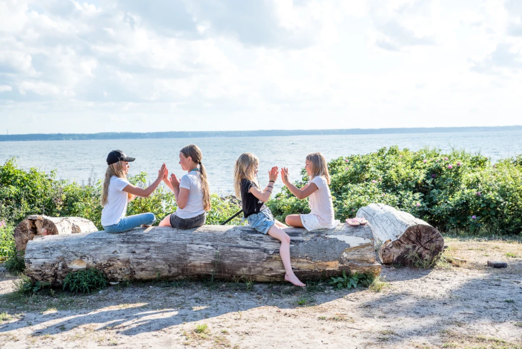 Fyra barn sitter på en trädstam vid havet och klappar händer med varandra