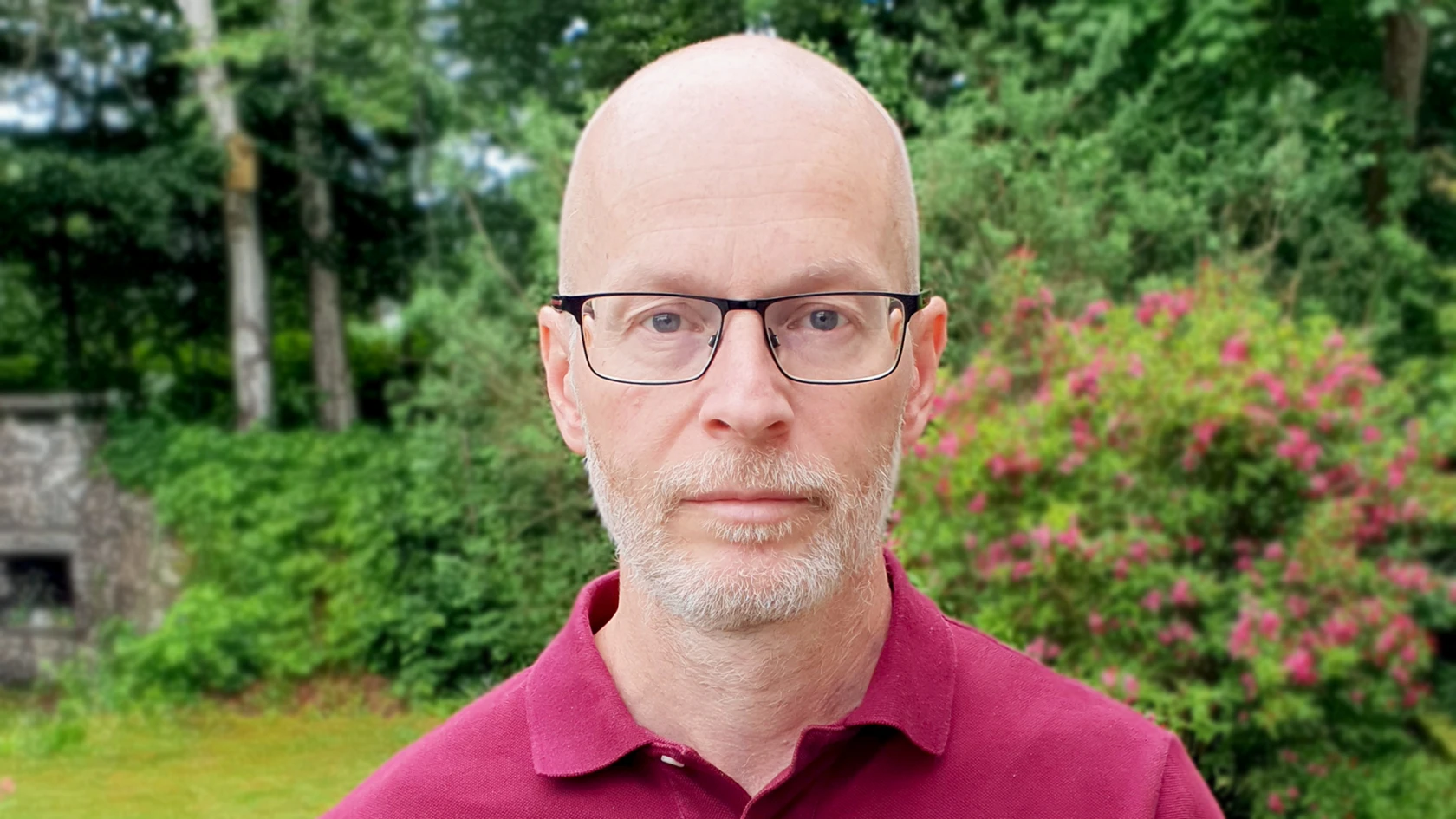 Flintskallig man med grått skägg, glasögon och röd pikettröja