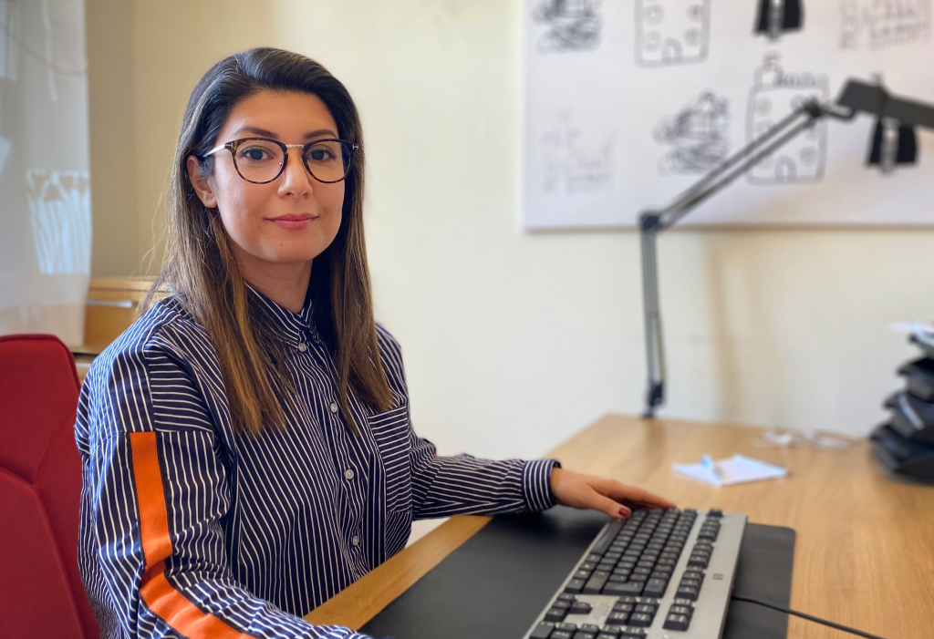Kvinna med långt mörkt hår och glasögon sitter vid ett skrivbord