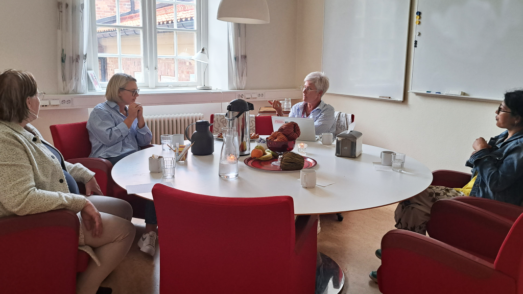 Fyra kvinnor sitter runt ett bord och har ett samtal.