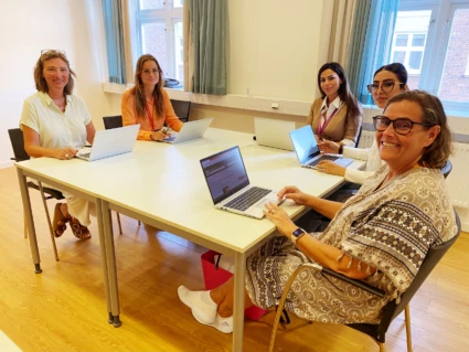 Sex kvinnor sitter runt ett bord med datorer tittar in i kameran och ler
