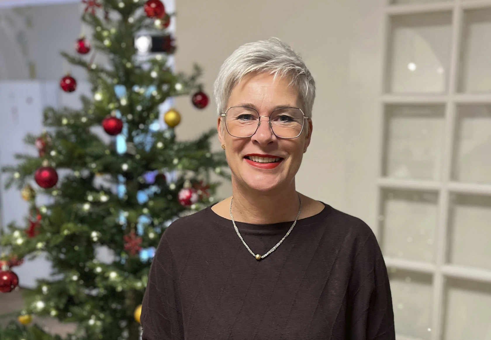 Leende medelålders kvinna med julgran i bakgrunden