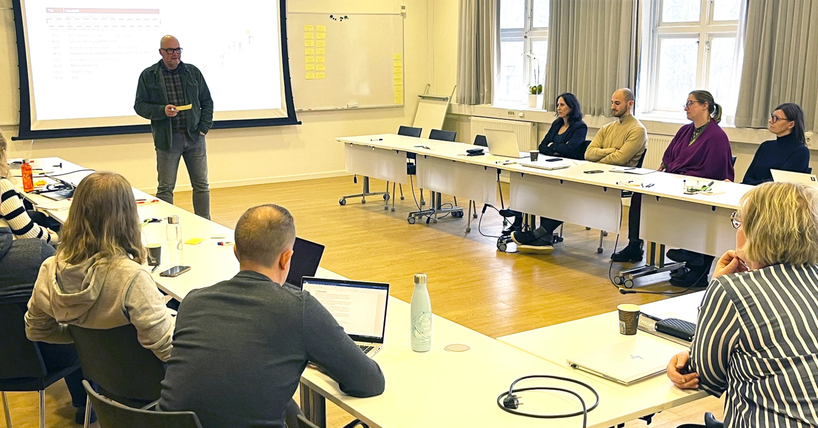 Medelålders man föreläser i ett konferensrum inför sittande män och kvinnor