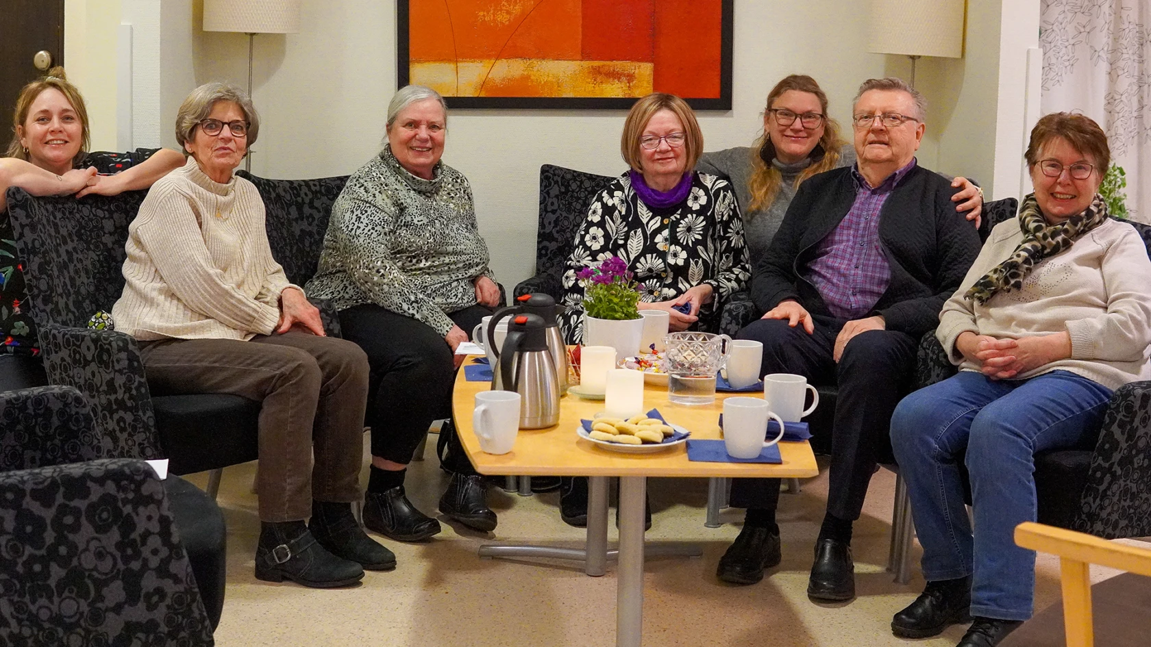 En grupp människor fikar och tittar in i kameran.