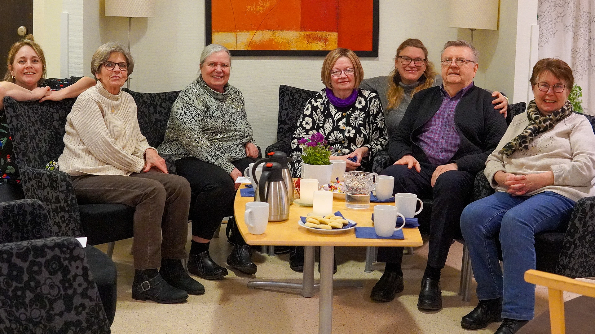 En grupp människor fikar och tittar in i kameran.