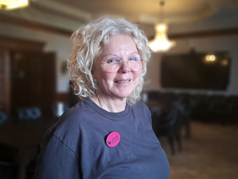 kvinna med glasögon, lockigt ljust hår i en pagefrisyr och sen mörkgrå tröja.