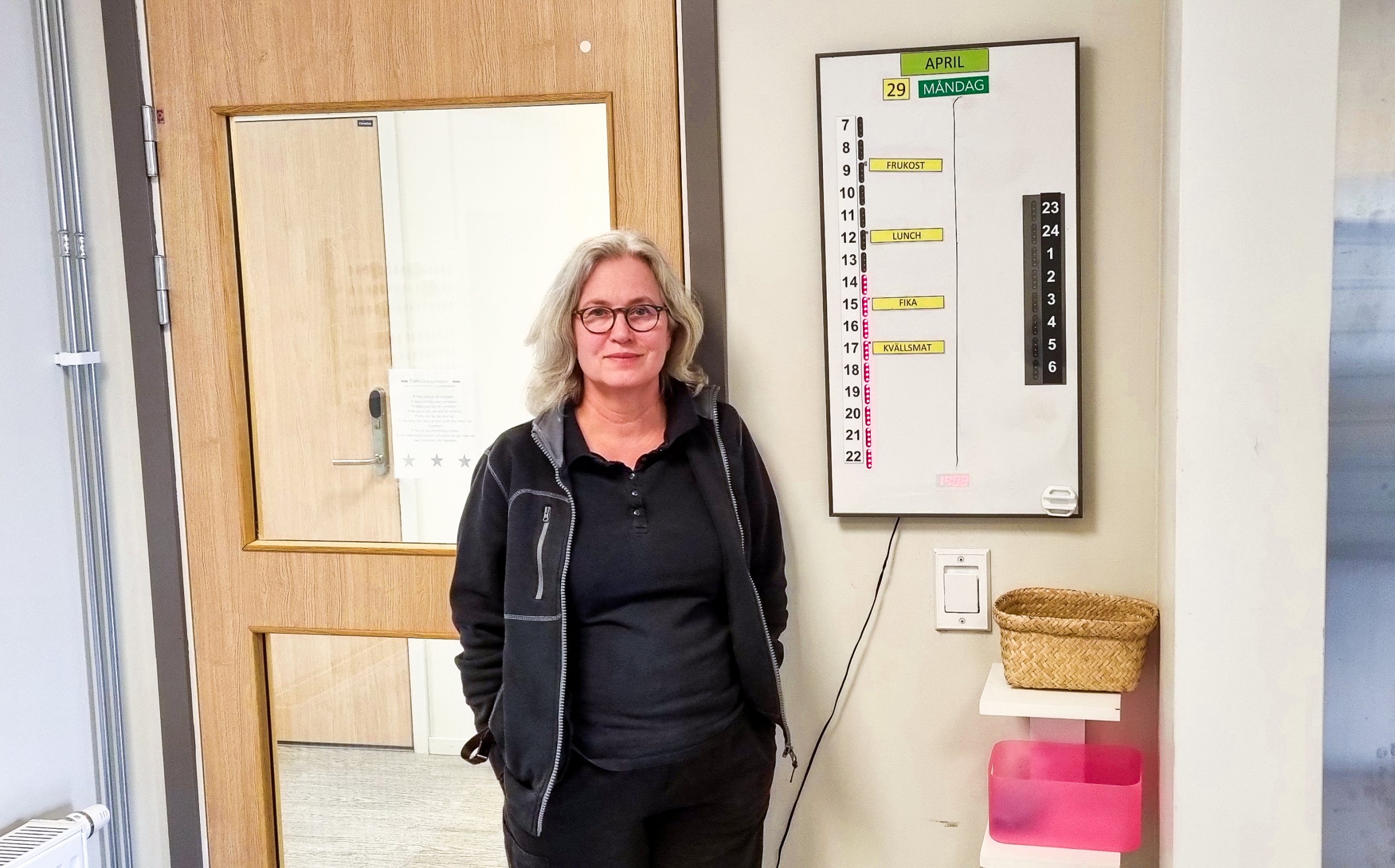 Kvinna står vid en dörr med glasfönster, tittar in i kameran och ler.