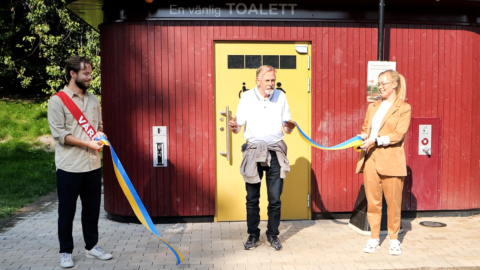 En man och en kvinna håller i ett bligult band som en man i mitten klipper av.