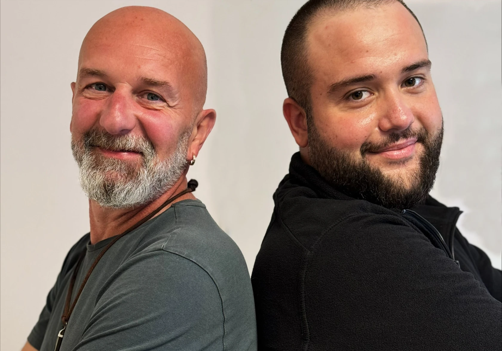 Två män som står rygg mot rygg tittar in i kameran och ser positiva ut