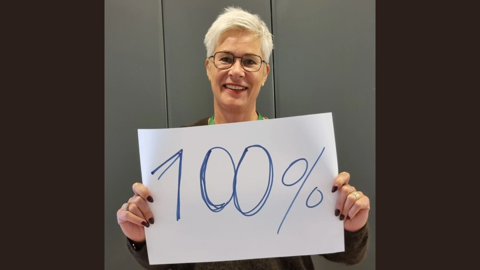 En person ler och håller upp en skylt med texten 100 procent.