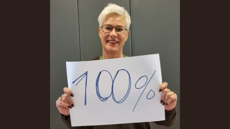 En person ler och håller upp en skylt med texten 100 procent.