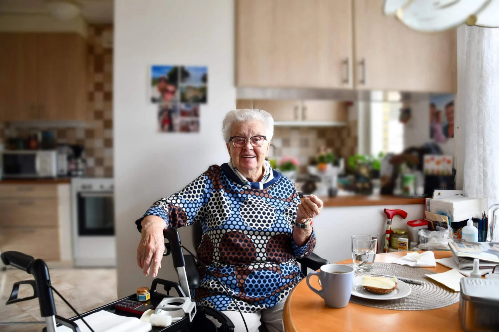 en kvinna sitter vid sitt köksbord och ser glad ut, tittar in i kameran