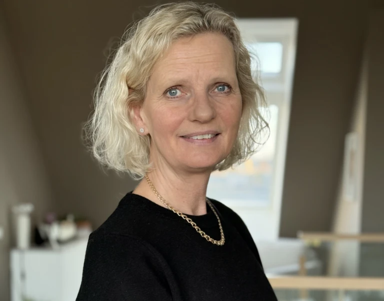 Kvinna med kort blont hår, tittar in i kameran och ler