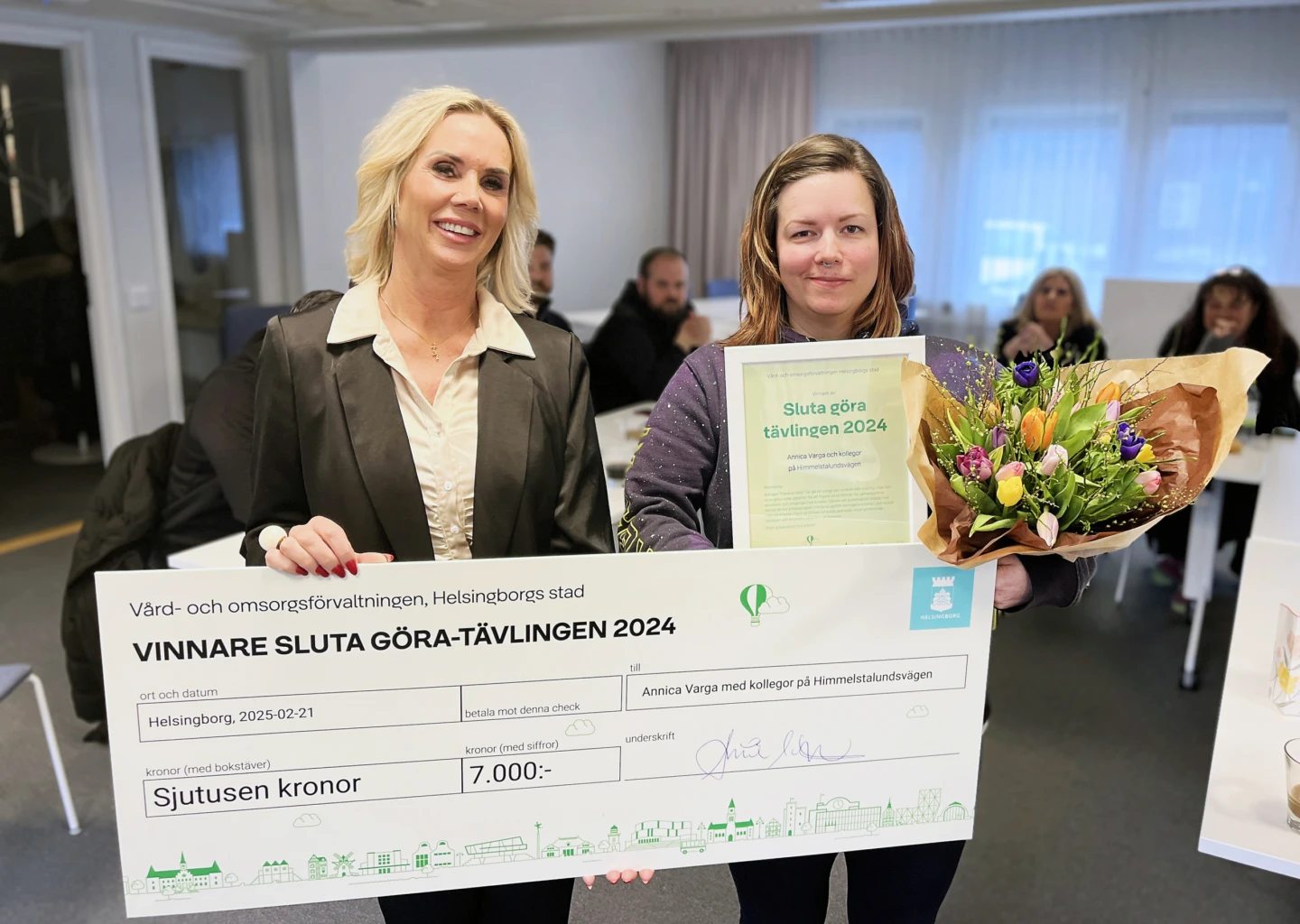 Två kvinnor med en prischeck, blombukett och diplom.