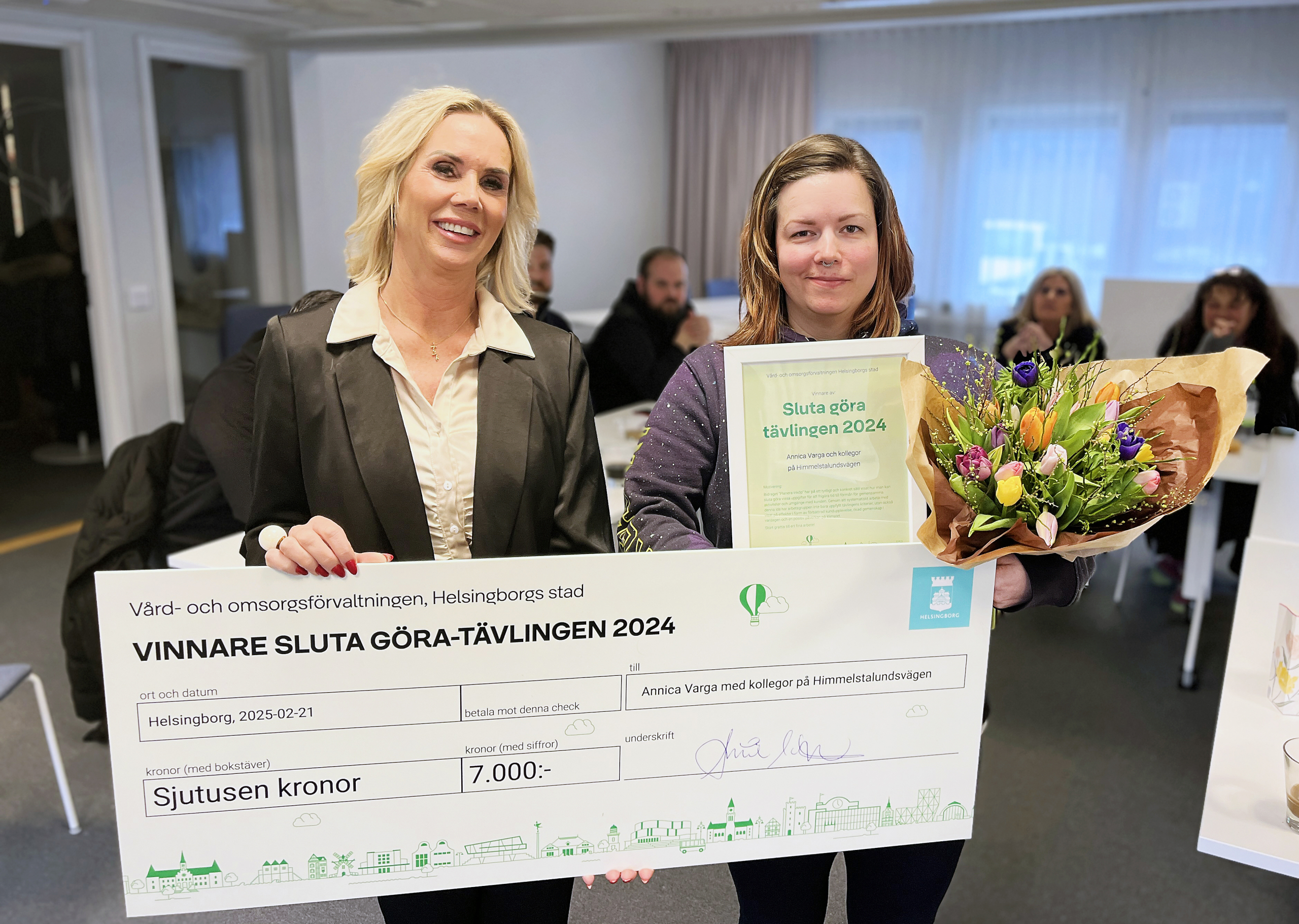Två kvinnor med en prischeck, blombukett och diplom.