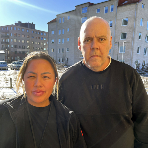 En medelålders man och en kvinna i 30-års åldern står tillsammans och tittar in i kameran.