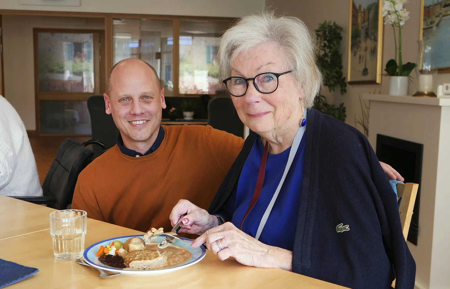 Man sitter på huk intill en äldre dam som äter sin lunch